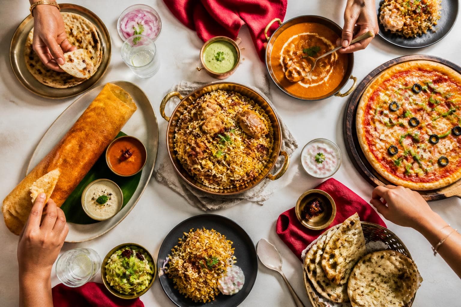 An overhead spread of Indian dishes including biryani, dosa, butter chicken, naan and fresh chutneys
